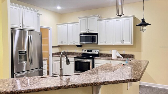 kitchen with a breakfast bar area, stainless steel appliances, pendant lighting, white cabinetry, and dark stone countertops