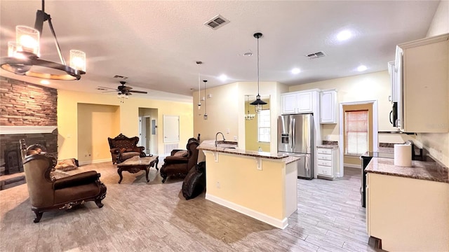 kitchen with appliances with stainless steel finishes, a stone fireplace, an island with sink, pendant lighting, and a breakfast bar