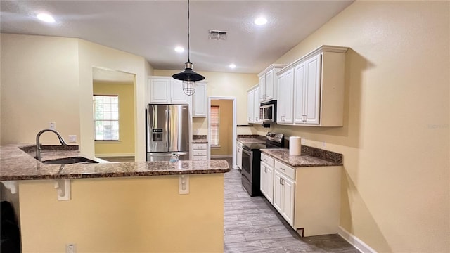 kitchen with appliances with stainless steel finishes, a breakfast bar, sink, white cabinetry, and dark stone countertops