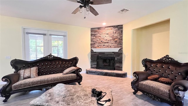 living room featuring ceiling fan, a stone fireplace, and wood-type flooring