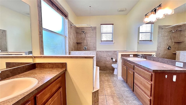 bathroom with tile patterned flooring, toilet, tile walls, vanity, and tiled shower