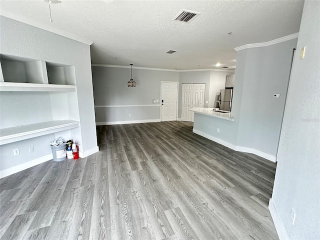 unfurnished living room with crown molding, built in features, a textured ceiling, and hardwood / wood-style flooring