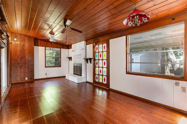 unfurnished living room with wooden ceiling, wooden walls, a brick fireplace, ceiling fan, and wood-type flooring