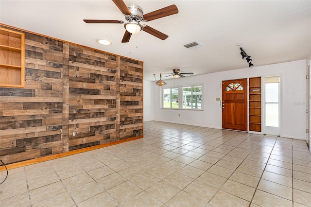 unfurnished living room with wood walls, ceiling fan, and light tile patterned flooring