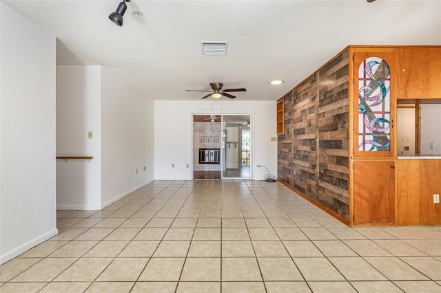 unfurnished living room with ceiling fan, a large fireplace, light tile patterned floors, and wooden walls