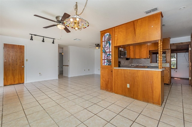 kitchen with ceiling fan with notable chandelier, light tile patterned flooring, kitchen peninsula, and tasteful backsplash