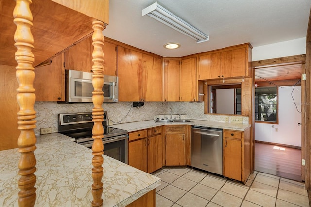 kitchen with kitchen peninsula, sink, light tile patterned floors, and stainless steel appliances