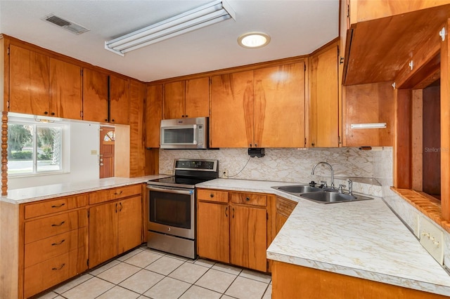 kitchen with backsplash, sink, light tile patterned floors, kitchen peninsula, and stainless steel appliances