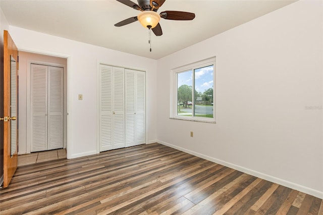 unfurnished bedroom featuring ceiling fan, dark hardwood / wood-style floors, and two closets