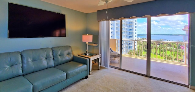 carpeted living room with ceiling fan and a water view