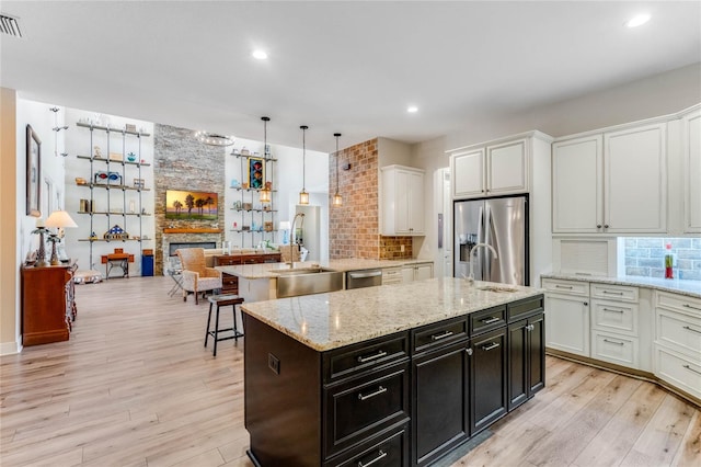 kitchen featuring hanging light fixtures, appliances with stainless steel finishes, a fireplace, a kitchen island, and light wood-type flooring