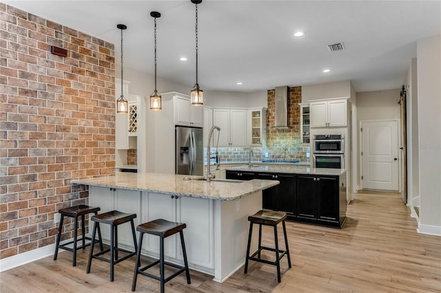 kitchen featuring a breakfast bar, wall chimney range hood, hanging light fixtures, light hardwood / wood-style floors, and stainless steel appliances