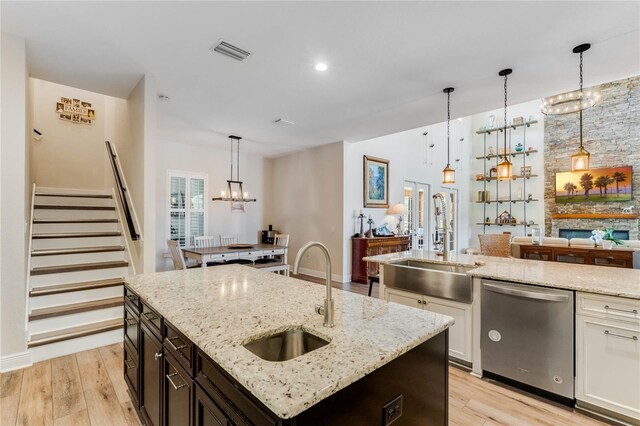 kitchen featuring stainless steel dishwasher, light hardwood / wood-style floors, sink, and a kitchen island with sink