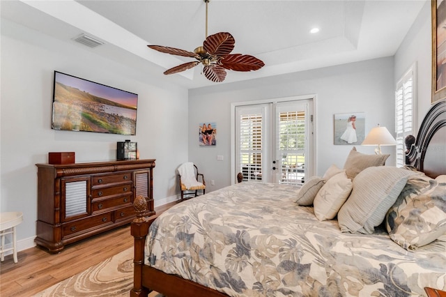 bedroom featuring access to exterior, french doors, a tray ceiling, ceiling fan, and light hardwood / wood-style floors