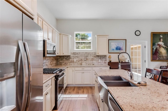 kitchen with sink, light hardwood / wood-style flooring, decorative backsplash, light stone countertops, and appliances with stainless steel finishes