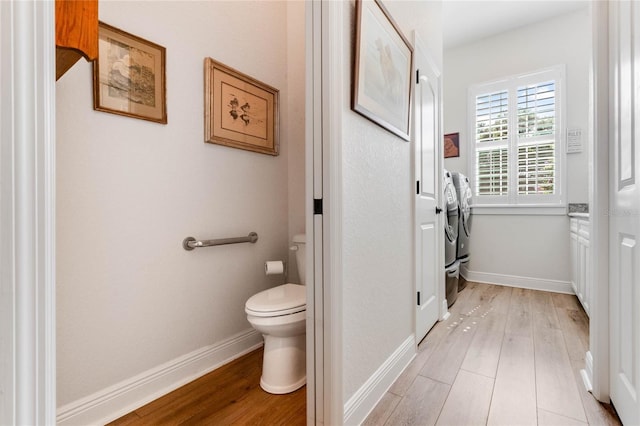 bathroom with washing machine and dryer, hardwood / wood-style floors, and toilet