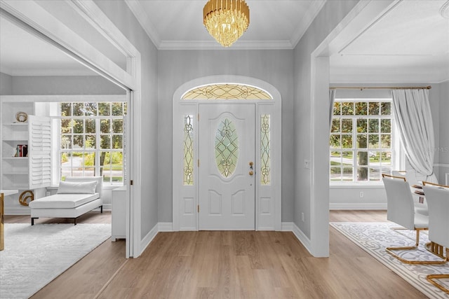 foyer with a wealth of natural light, crown molding, a notable chandelier, and light wood-type flooring