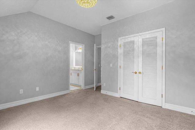 unfurnished bedroom featuring carpet, ensuite bath, a closet, and lofted ceiling