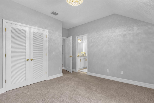 unfurnished bedroom with a textured ceiling, ensuite bathroom, light carpet, and vaulted ceiling