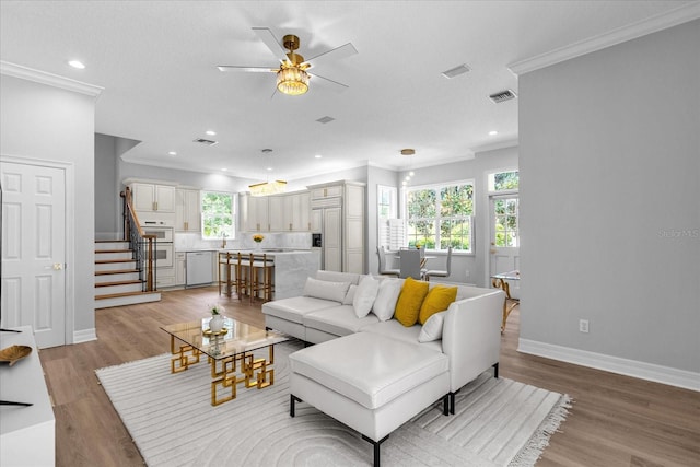 living room with crown molding, ceiling fan, and light wood-type flooring