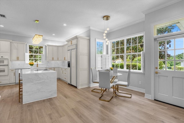 kitchen with light stone counters, backsplash, decorative light fixtures, paneled built in fridge, and light wood-type flooring