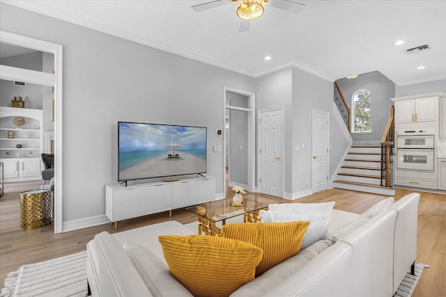 living room featuring built in shelves, light hardwood / wood-style flooring, ceiling fan, and ornamental molding