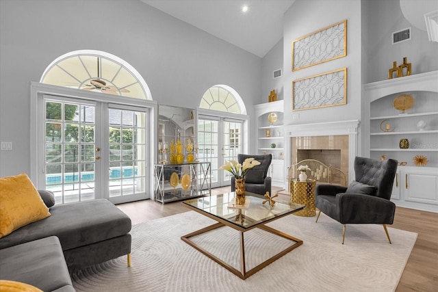 living area with high vaulted ceiling, french doors, built in features, light hardwood / wood-style floors, and a tiled fireplace