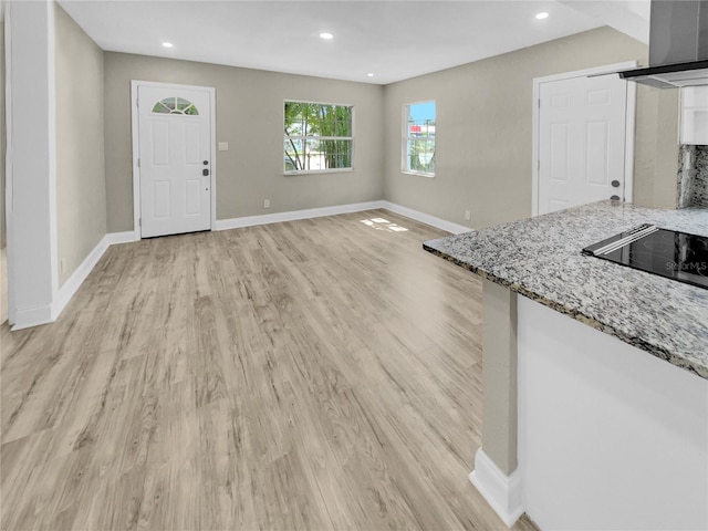 interior space featuring light stone countertops, black electric stovetop, light wood-type flooring, and range hood