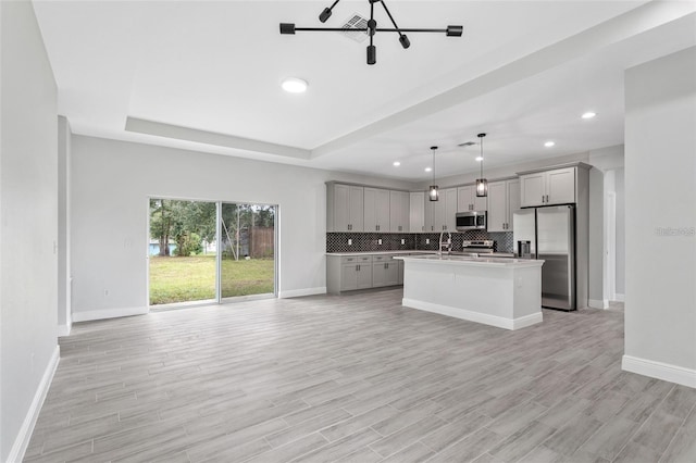 kitchen featuring hanging light fixtures, a center island with sink, stainless steel appliances, backsplash, and a raised ceiling