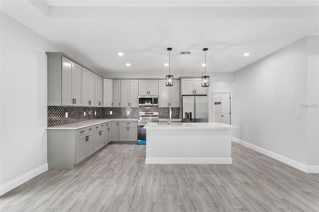 kitchen featuring stainless steel appliances, hanging light fixtures, an island with sink, and gray cabinets