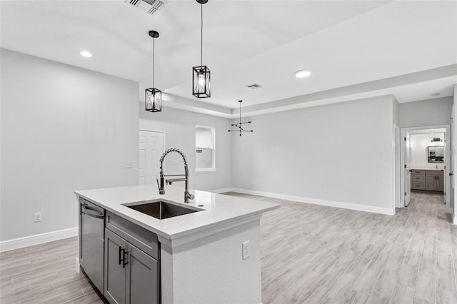 kitchen with light wood-type flooring, gray cabinetry, an island with sink, decorative light fixtures, and sink