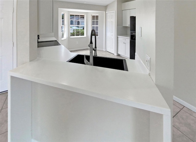 kitchen featuring sink, black fridge, light tile patterned flooring, kitchen peninsula, and white cabinets