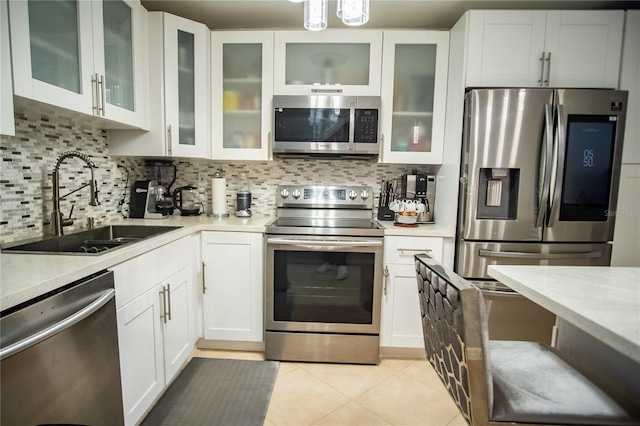 kitchen with appliances with stainless steel finishes, white cabinets, sink, light tile patterned floors, and decorative backsplash