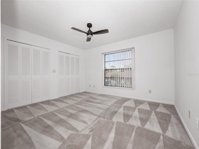 unfurnished bedroom with ceiling fan, light colored carpet, a textured ceiling, and multiple closets