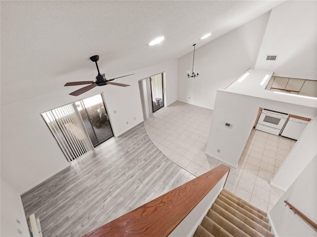 interior space with ceiling fan with notable chandelier, lofted ceiling, a textured ceiling, and light tile patterned floors