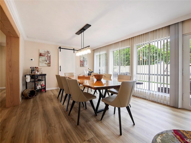 dining room with a barn door, baseboards, ornamental molding, and light wood finished floors