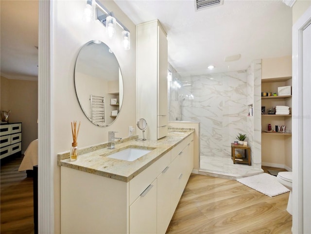 bathroom with a marble finish shower, visible vents, toilet, wood finished floors, and vanity