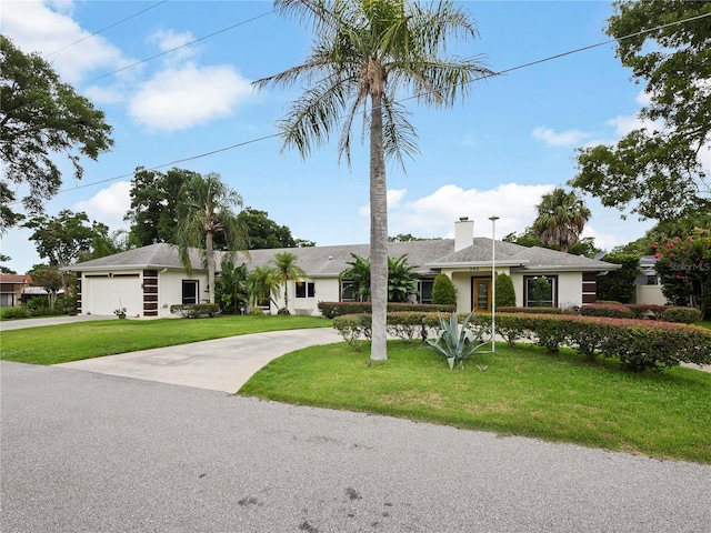 ranch-style home with a front yard, a garage, driveway, and a chimney