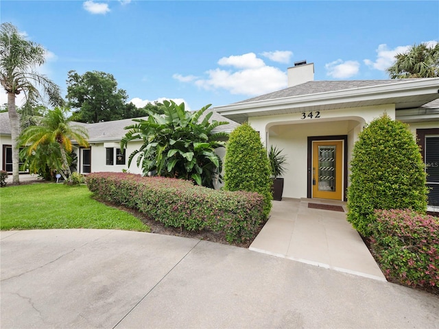 doorway to property featuring stucco siding, a lawn, and a chimney