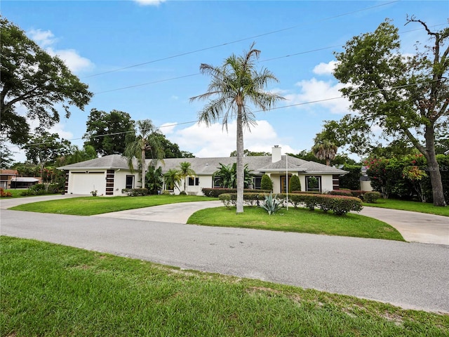 single story home with a chimney, an attached garage, concrete driveway, and a front lawn