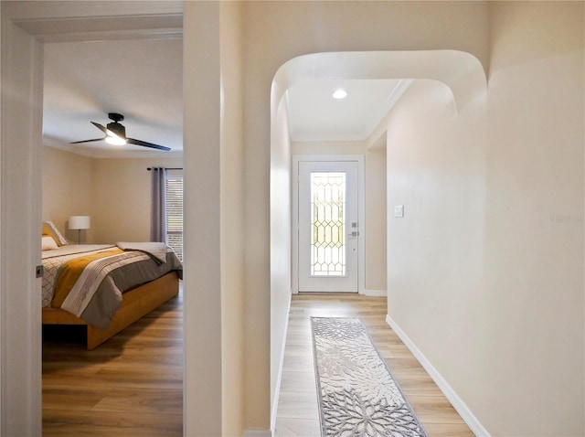 doorway to outside with baseboards, ornamental molding, light wood-style floors, arched walkways, and a ceiling fan