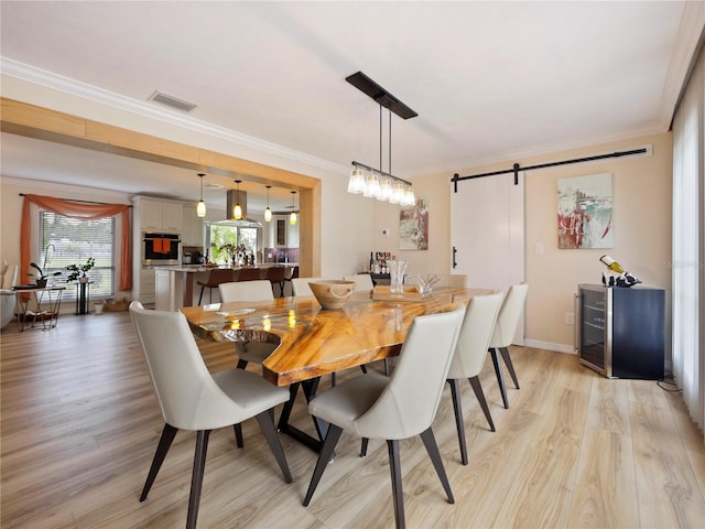 dining area with visible vents, baseboards, light wood-style floors, crown molding, and a barn door