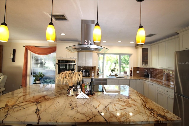 kitchen with oven, visible vents, freestanding refrigerator, island range hood, and decorative backsplash