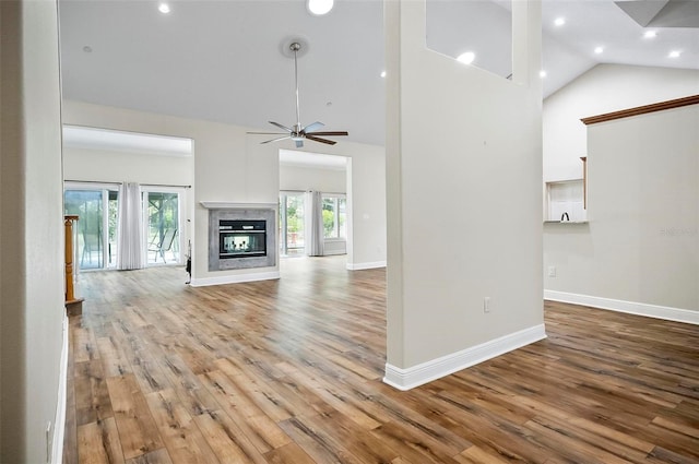 unfurnished living room with baseboards, a multi sided fireplace, high vaulted ceiling, and wood finished floors