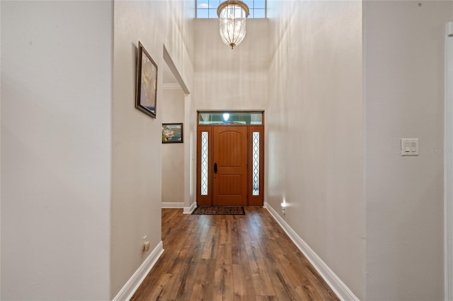 foyer entrance with a chandelier, baseboards, a high ceiling, and wood finished floors