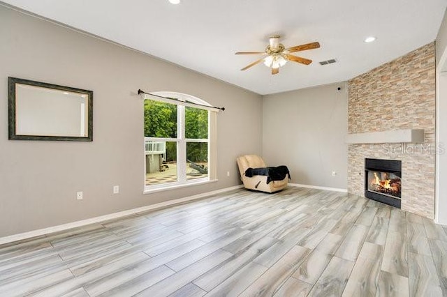 unfurnished room with ceiling fan, a stone fireplace, and light hardwood / wood-style flooring