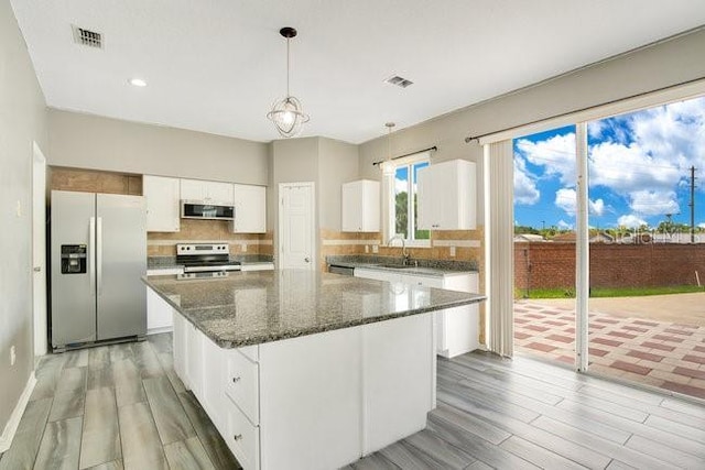 kitchen featuring pendant lighting, a center island, sink, white cabinetry, and stainless steel appliances