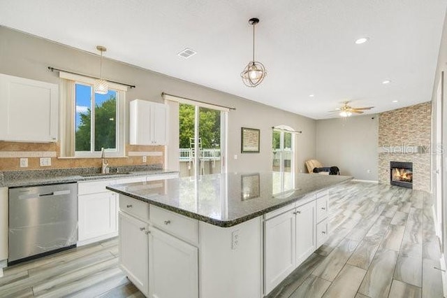 kitchen featuring dishwasher, sink, hanging light fixtures, a stone fireplace, and dark stone counters