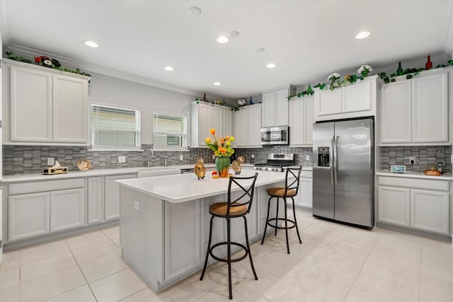 kitchen featuring ornamental molding, a breakfast bar, stainless steel appliances, white cabinetry, and a kitchen island