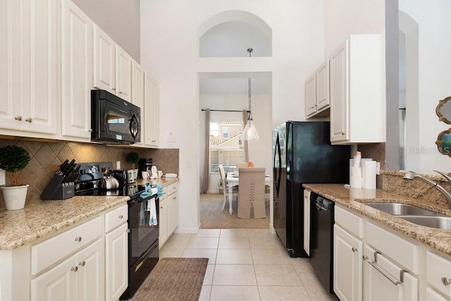 kitchen with light stone counters, white cabinetry, black appliances, sink, and light tile floors